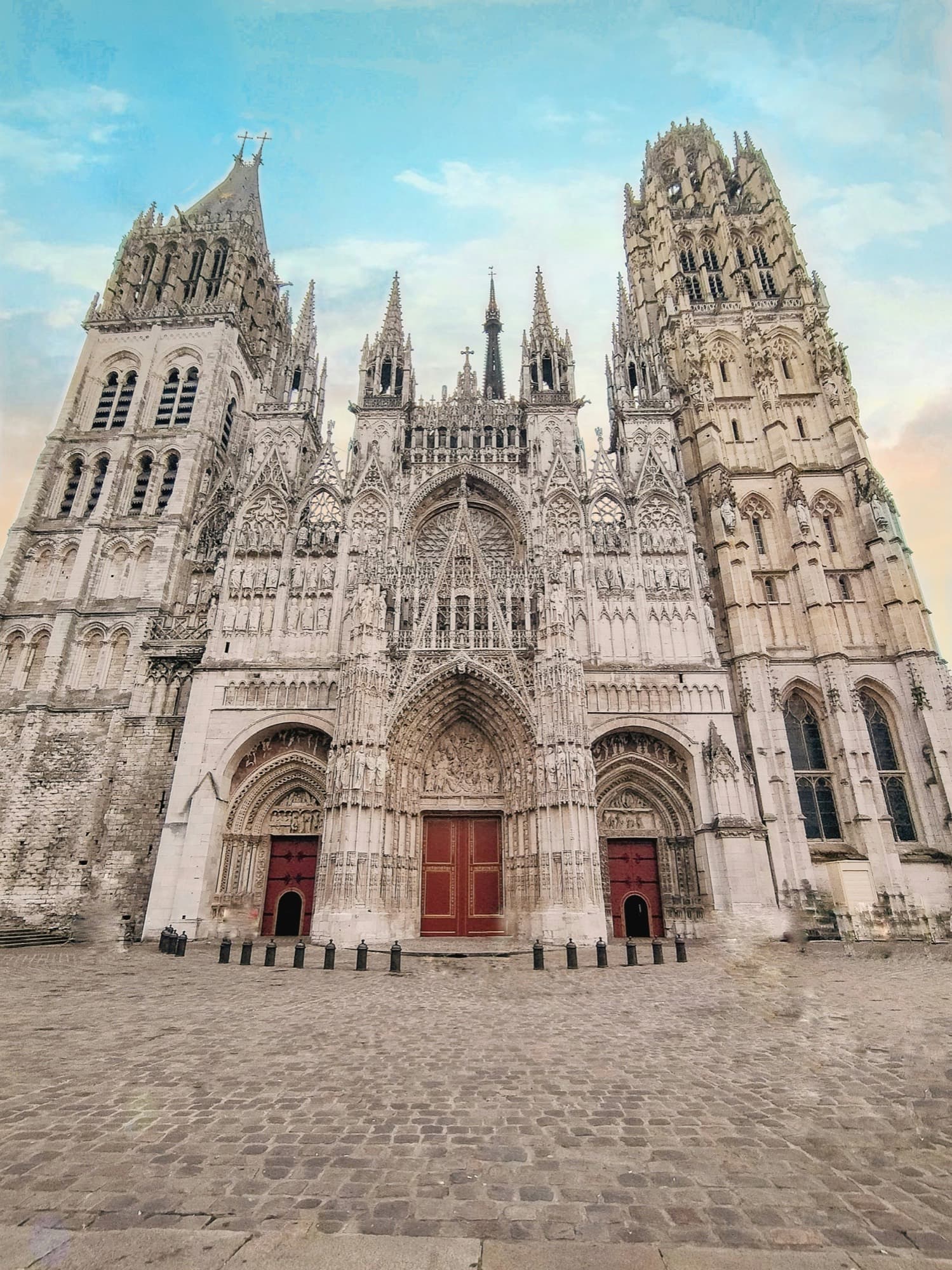 A pale Gothic cathedral facade with twin towers, a rose window, and red doors.