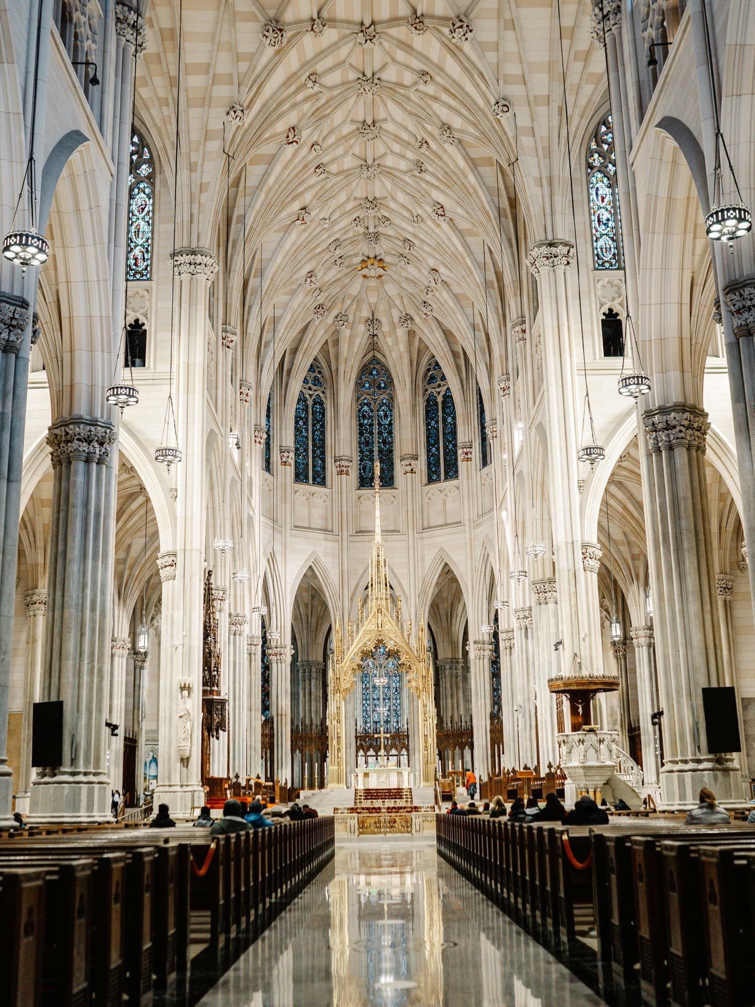 A pale stone nave with a vaulted ceiling, stained glass, and pews leading to the altar.