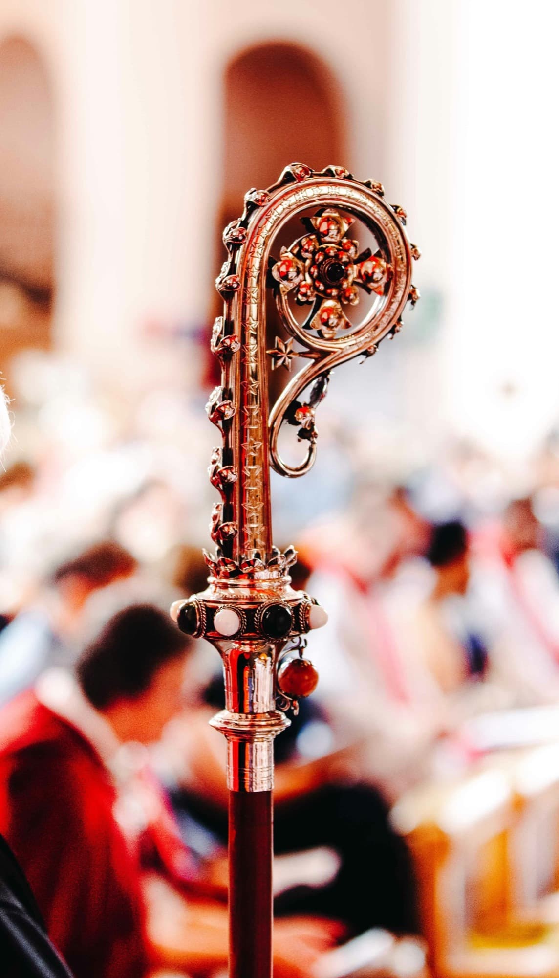 The jeweled crook of a bishop's crozier, with a congregation seated behind it.